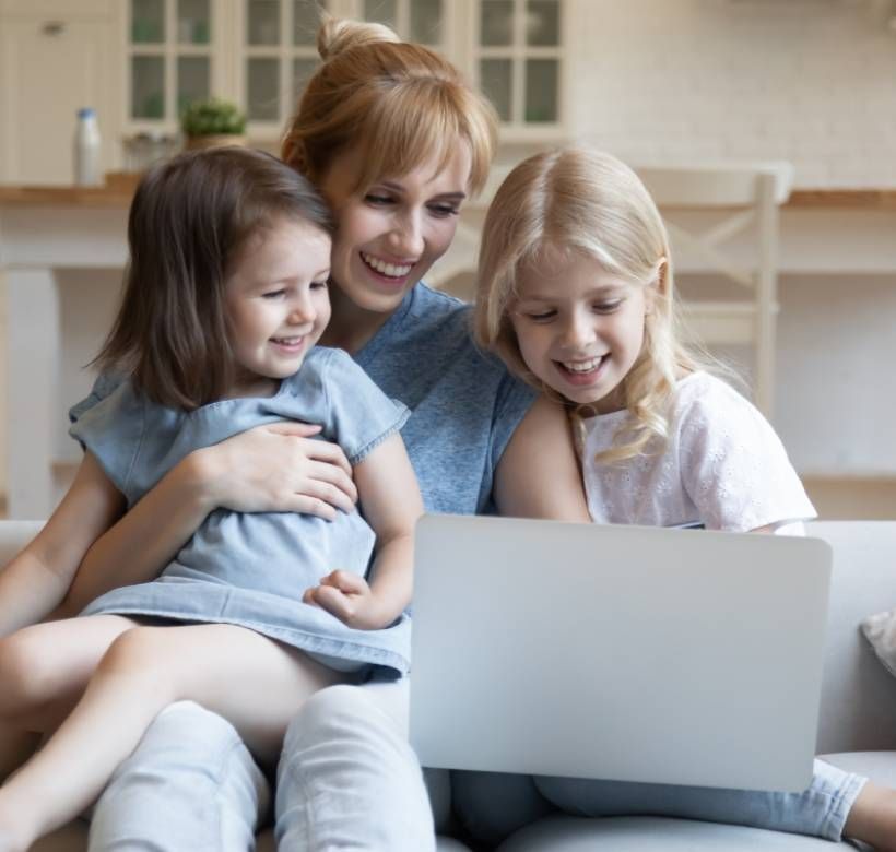 A smiling mother and her two young daughters looking at a laptop computer screen.