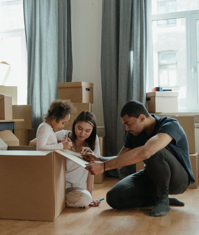 A mother, father and young girl labeling moving boxes in their living room.