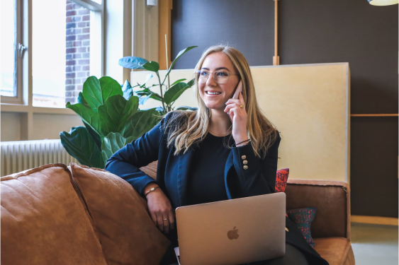 Woman in a suit jacket talking on her phone as she sits on an office sofa.