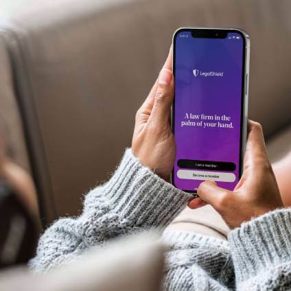 Woman relaxing on a sofa and looking at the LegalShiel app screen that reads: A law firm in the palm of your hand.