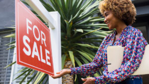 Agente inmobiliario colgando un cartel de venta frente a una casa.