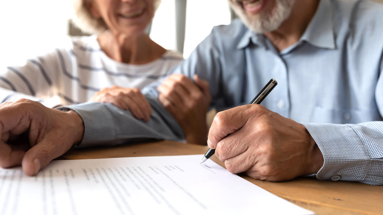 Un hombre firma un contrato de arrendamiento mientras su esposa observa.