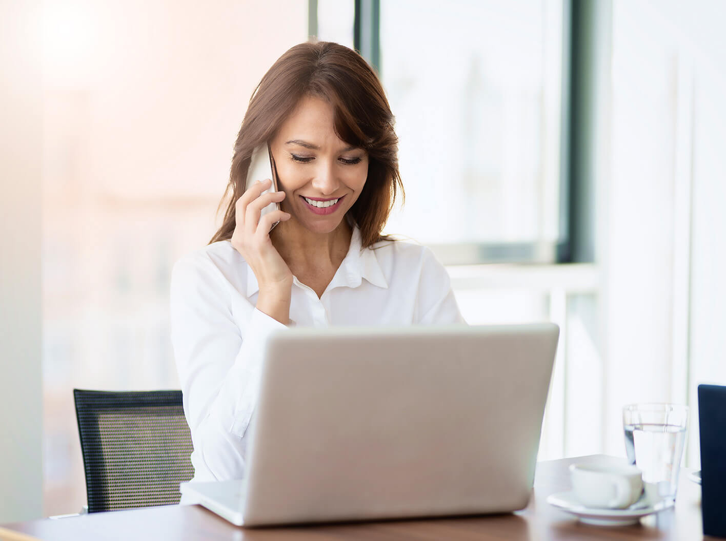 A woman is talking on the phone while sitting in front of her computer