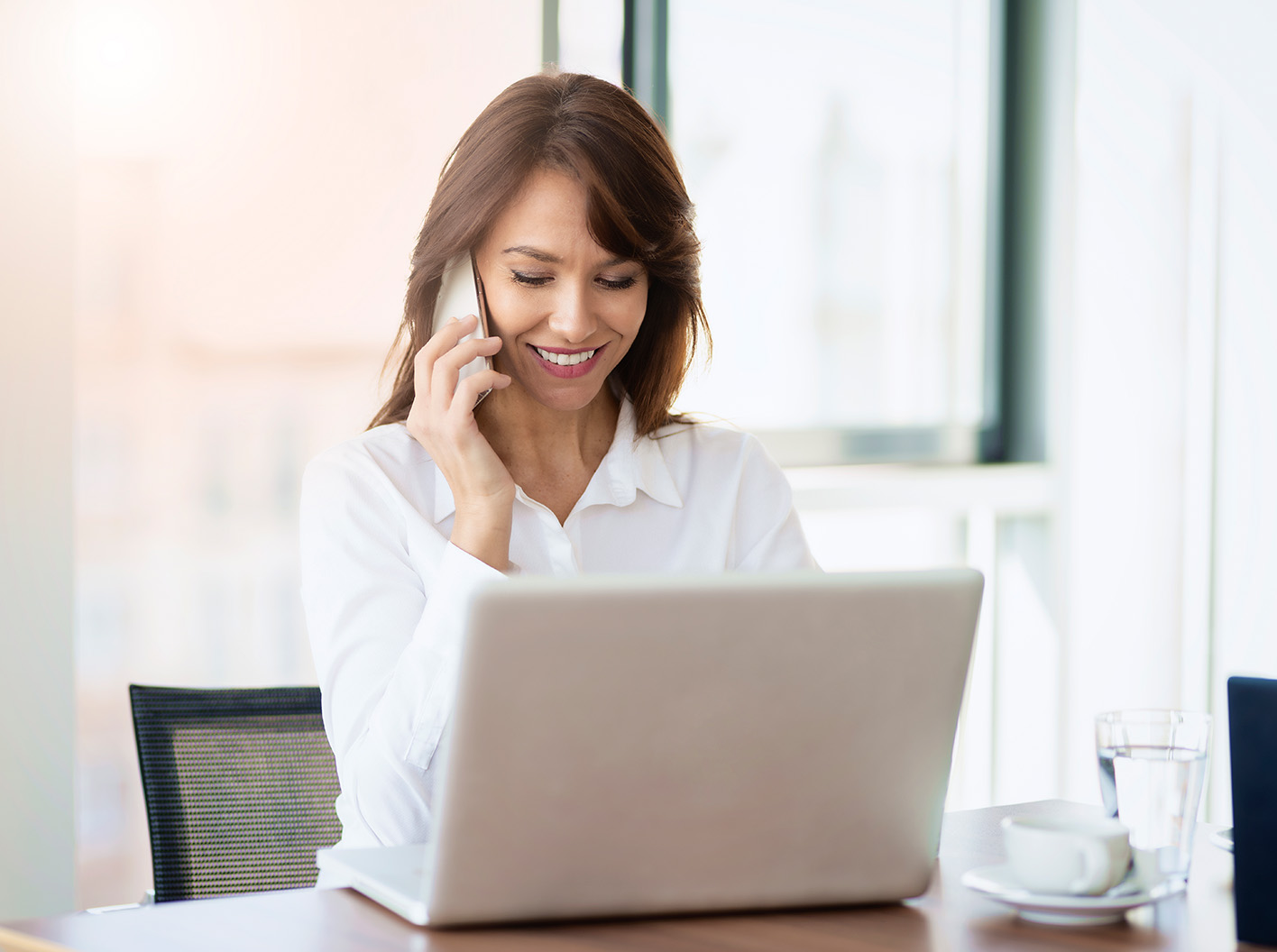 Business woman talking on th phone and looking at a laptop computer screen.