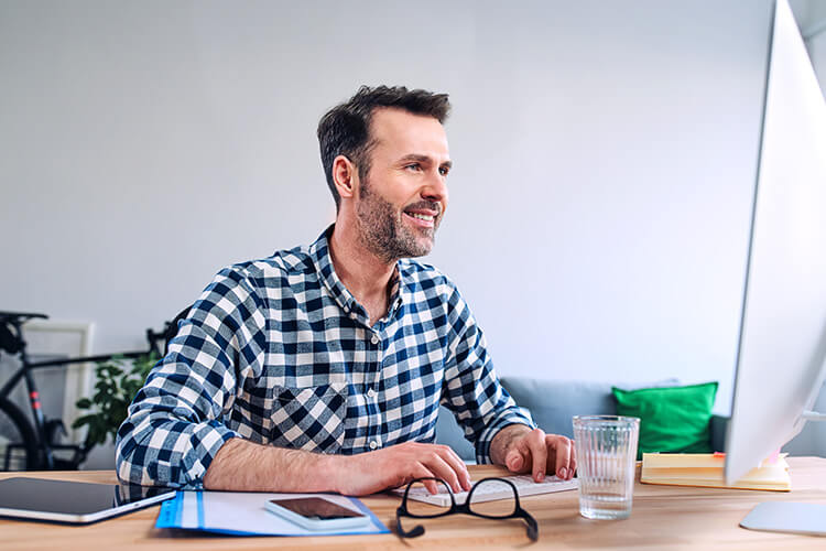 Employee smiling as he works at his desk while looking at a computer monitor.