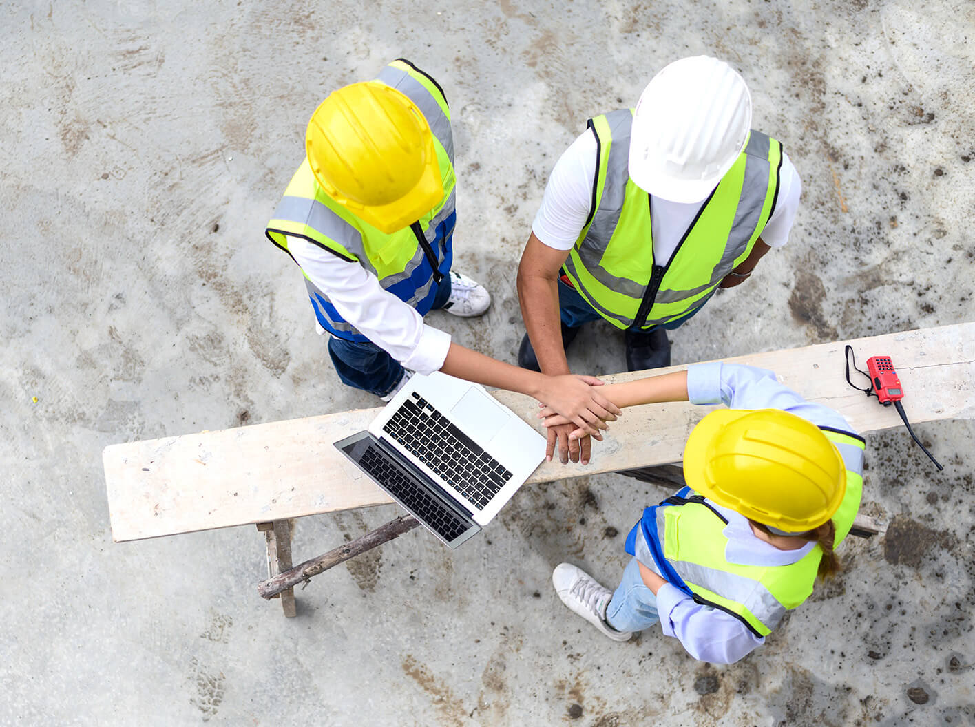 3 construction site workers stacking their hands in agreement and solidarity.