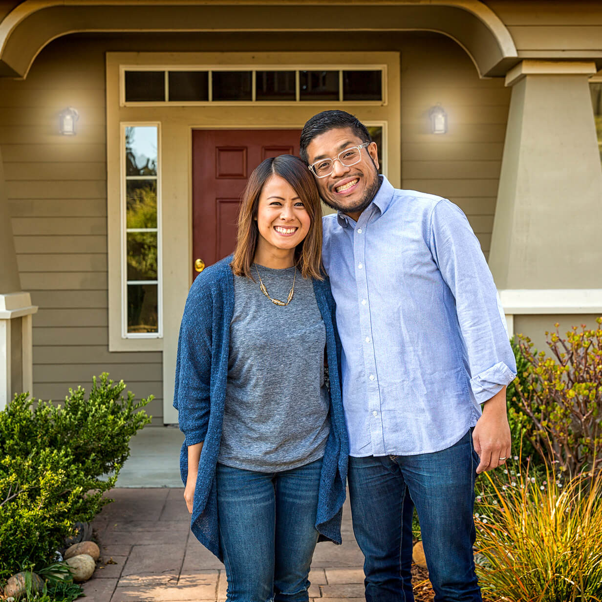 A couple is standing out in front of a house with their arms around each other.