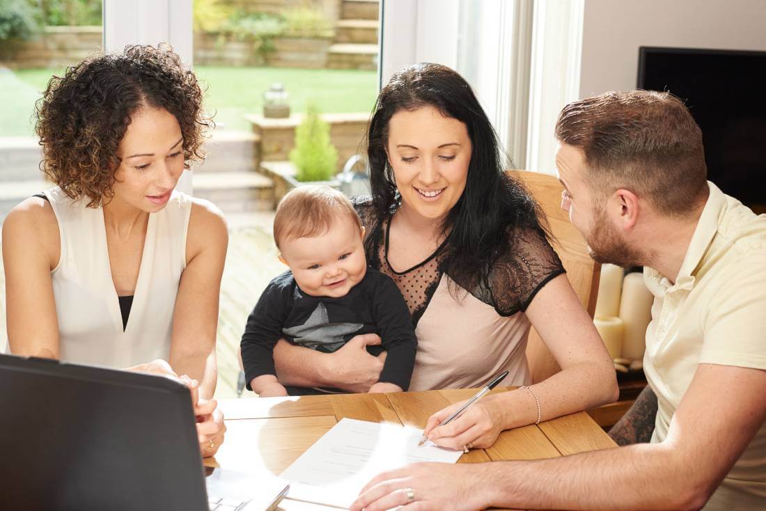 Mother signing a daycare contract as her baby, husband and daycare employee looks on.