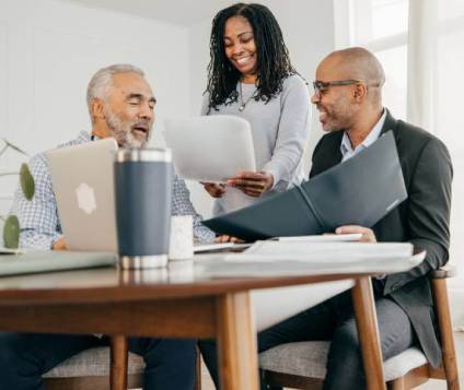 Woman smiling as she holds couple's estate planning documents while standing next to seated husband and lawyer.