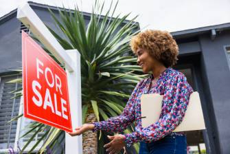 Real estate agent hanging a For Sale sign in front of a house.