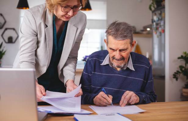 An elderly man is signing end-of-life legal documents with the assistance of his LegalShield lawyer.