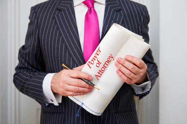 A lawyer in a stripped suit and pink tie holing a Power of Attorney document and ink pen.