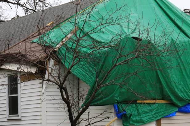 House roof damaged by a hurricane. A green tarp is covering roof damage.